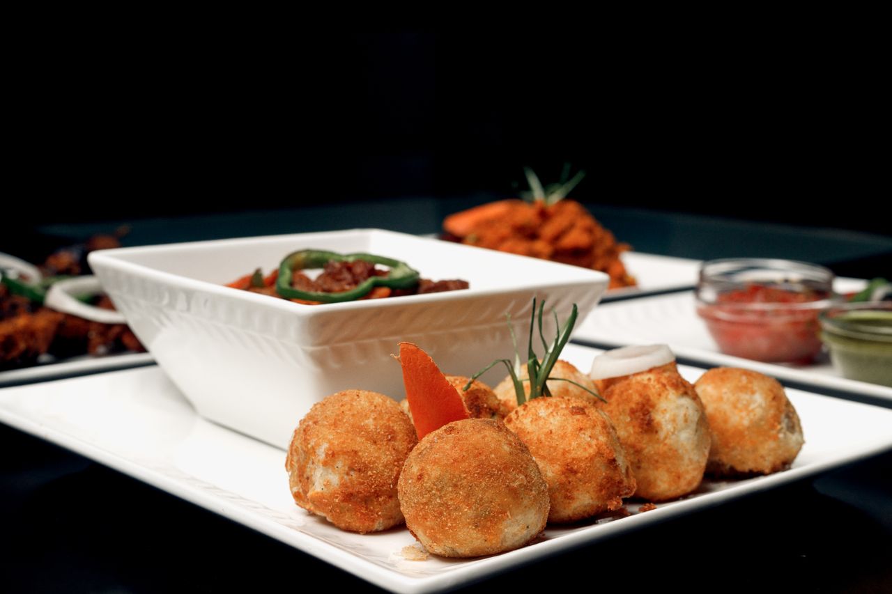 Crispy golden appetizer balls served with a savory dish on a white plate against a dark background.